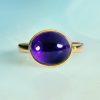 Oval amethyst cabochon (4.46ct) in 18ct yellow gold front view on green background