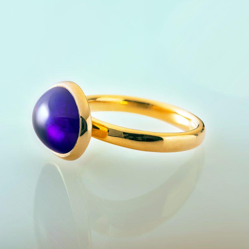 Oval amethyst cabochon (4.46ct) set in 18ct yellow gold. Side profile on green background.