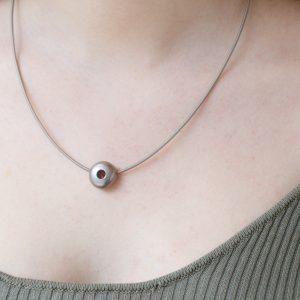 Stainless steel necklace with round lab-grown madeira topaz pendant in matt steel. shown on model's neck.