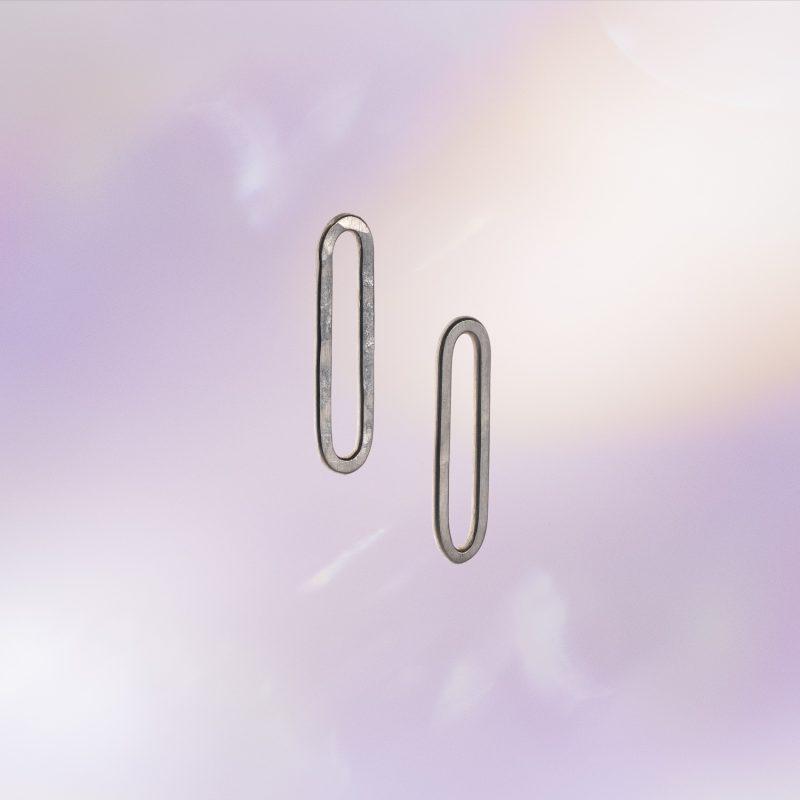 Pair of elongated oval link-shaped stud earrings in textured silver, shown against a soft pastel background.