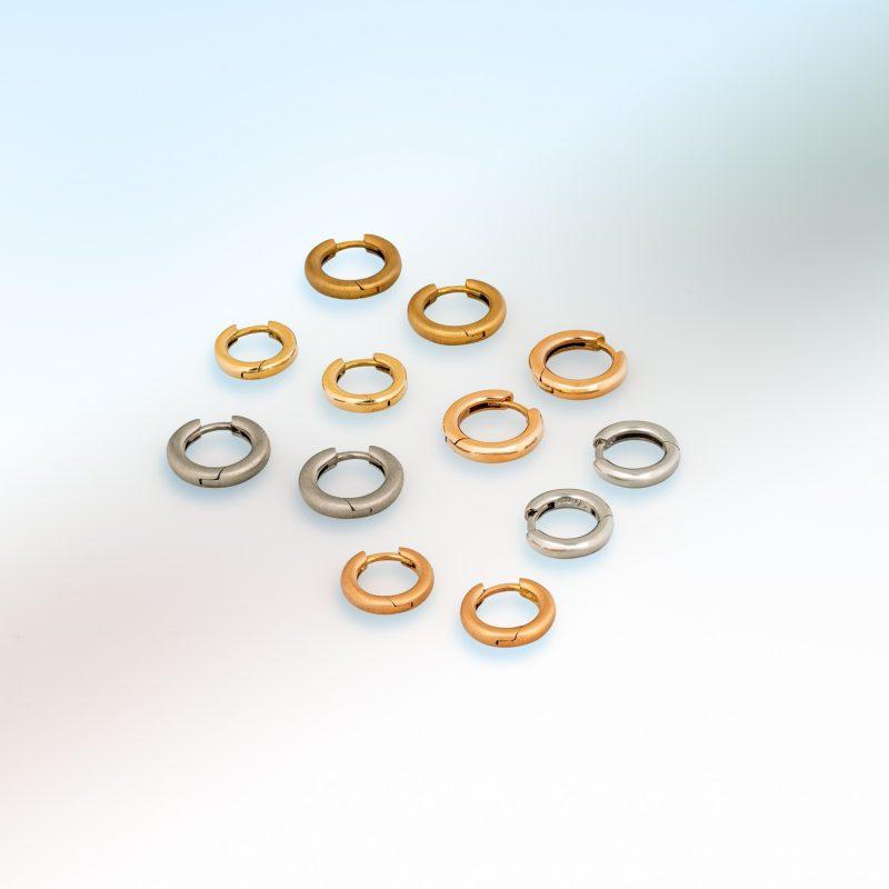 Group shot of small hinged hoop earrings in platinum, 18ct yellow gold, and 18ct rose gold, arranged on a soft gradient background