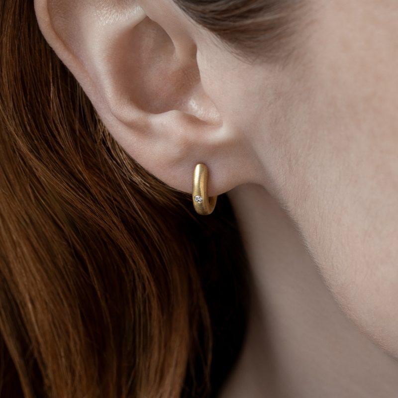 solid 18ct yellow gold hinged hoop earring with white brilliant cut diamond, shown on model's ear. Earring sits hugging the earlobe.